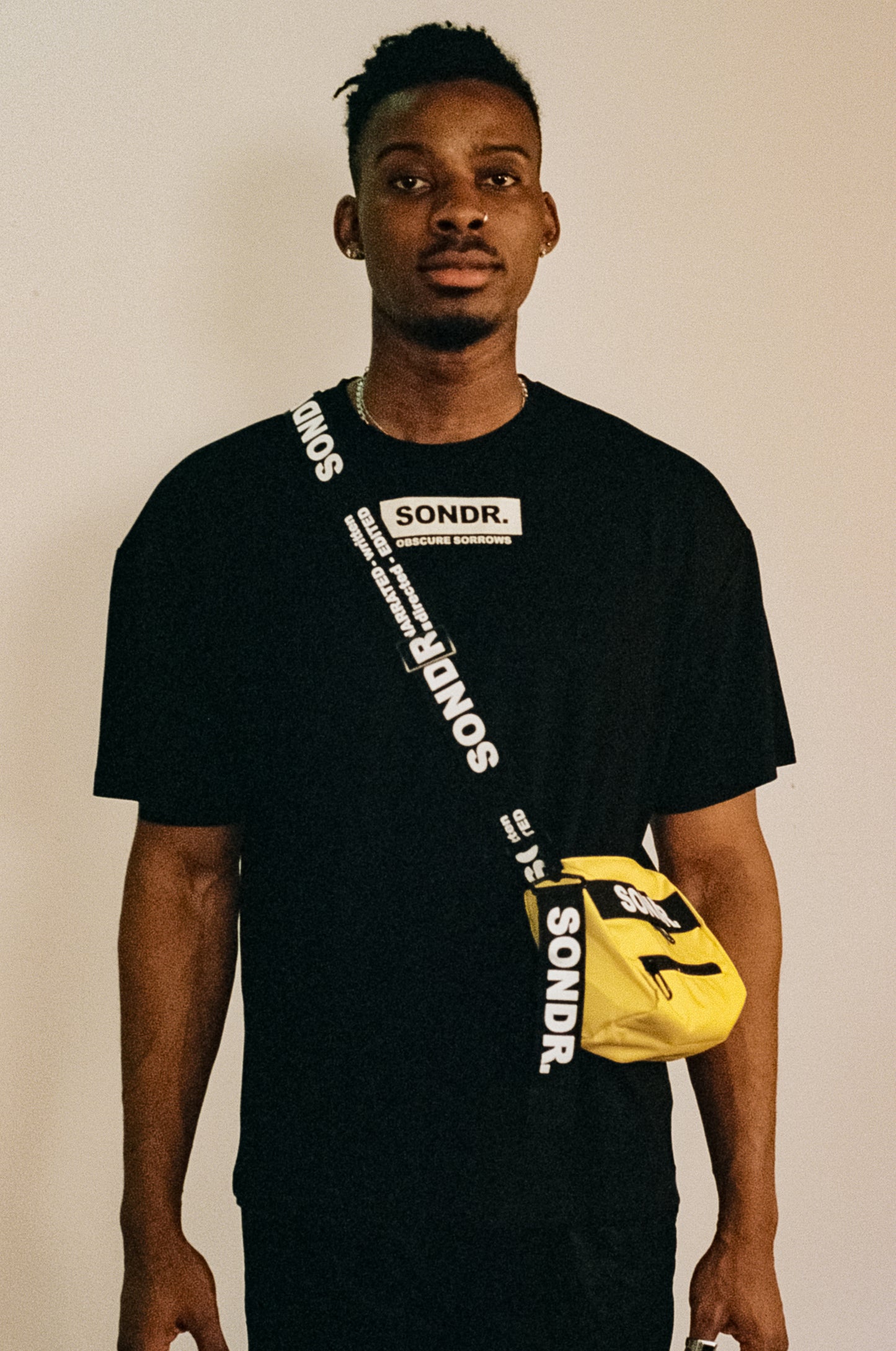 Image of Joseph Peters from Project Peters wearing a Yellow SONDR. Side Bag & Black SONDR. Logo T-shirt with his hands by his side.