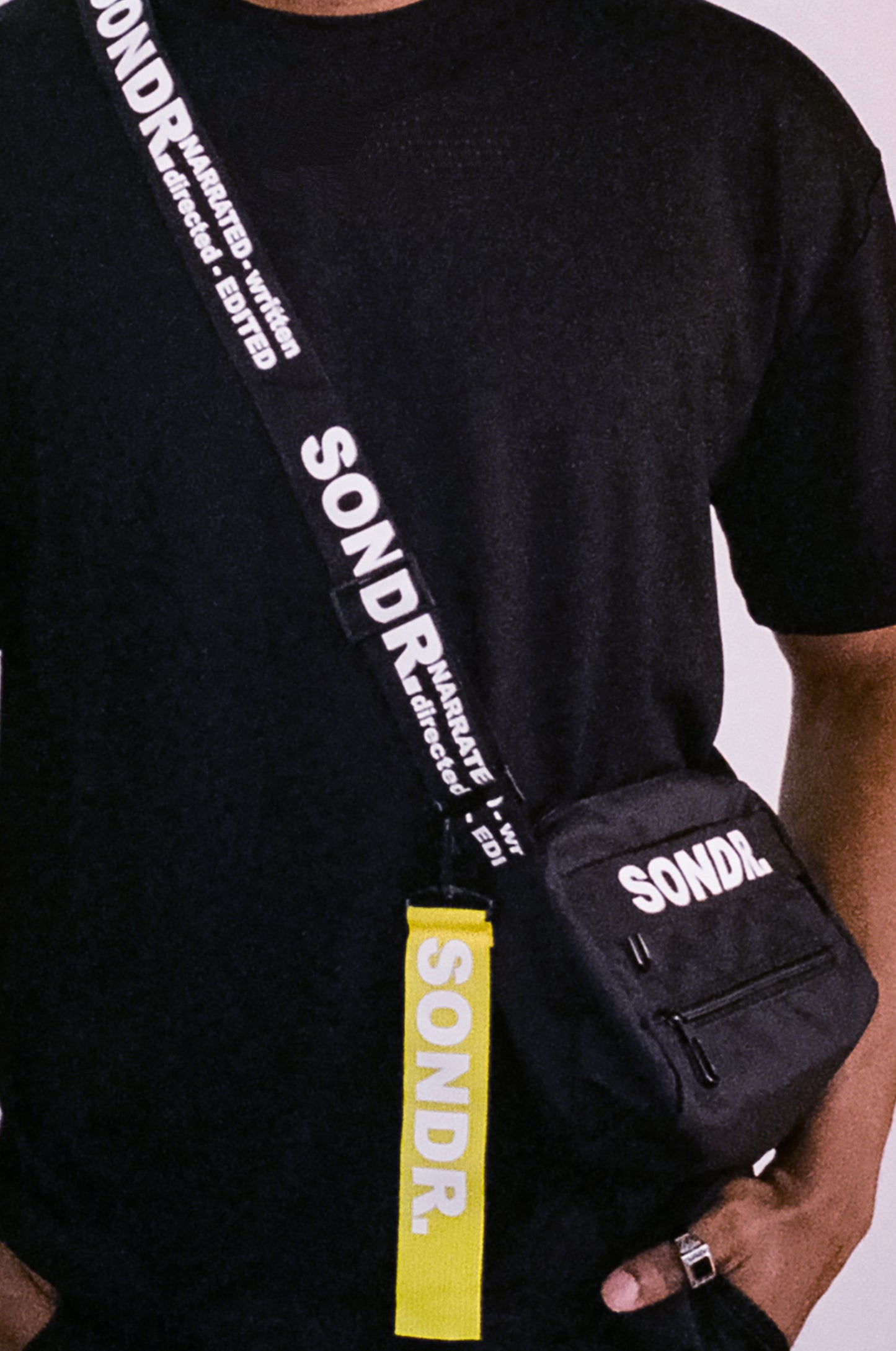 Close up shot of SONDR. Black Side Bag Product Image. Showing shoulder trap print & yellow tag